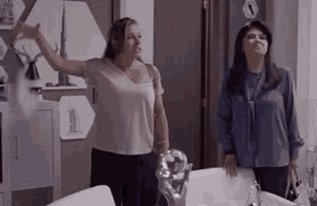 two women are standing next to each other in a living room . one of the women is holding a statue .