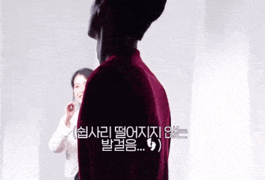 a man in a red shirt stands in front of a white wall with korean writing on it