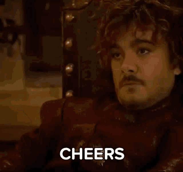 a man with a mustache is sitting in a chair with the word cheers written on his face .