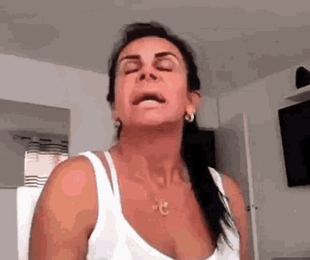 a woman in a white tank top is sitting in a chair with her eyes closed .