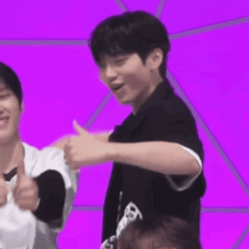 a man is giving a thumbs up sign in front of a purple background while another man looks on .