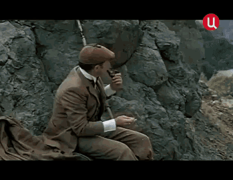a man in a suit and hat is sitting on a rock and looking up .