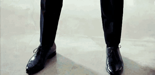a man wearing a suit and black shoes is standing on a tiled floor .