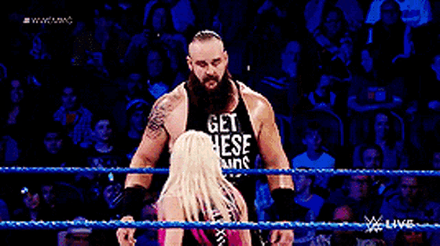 a man in a tank top that says get these hands is standing next to a woman in a wrestling ring