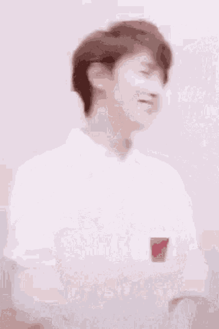 a man in a white shirt is standing in front of a white wall and looking at the camera .
