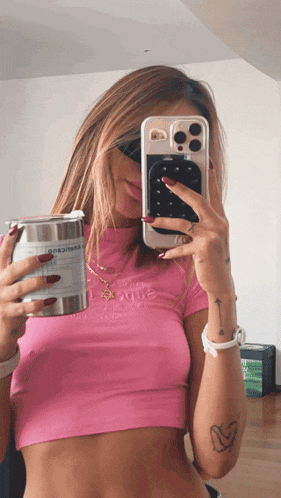 a woman in a pink crop top is taking a picture of herself with her phone