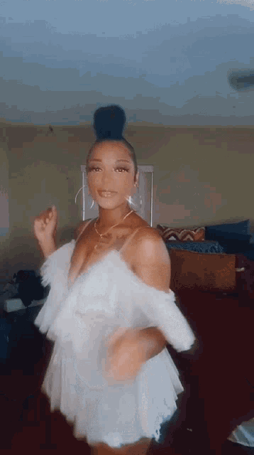 a woman in a white dress is dancing in a living room with a bun in her hair .
