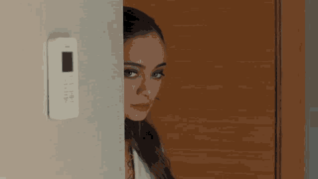 a woman peeking out from behind a wall behind a remote control