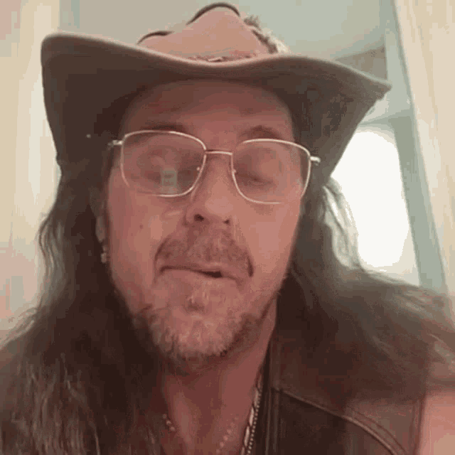 a man with long hair and glasses wearing a cowboy hat