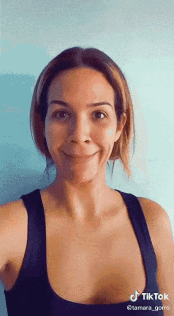 a woman in a black tank top is smiling and has a tiktok watermark on her face