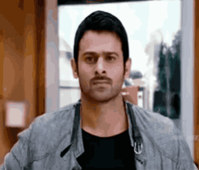 a man with a mustache is standing in front of a window .