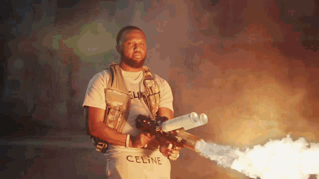 a man in a celine t-shirt is holding a flame thrower