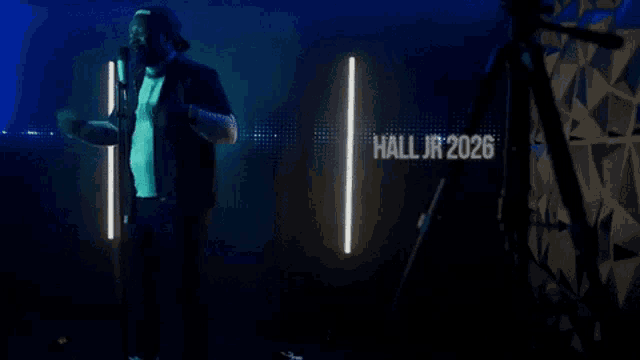 a man singing into a microphone with hall jr 2026 written in white