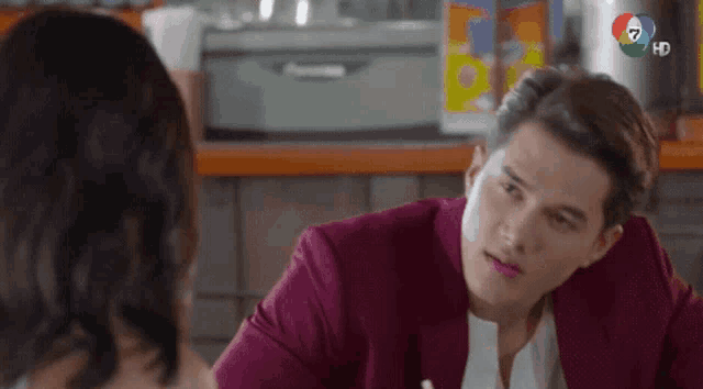 a man in a red suit is sitting at a table talking to a woman in a restaurant .
