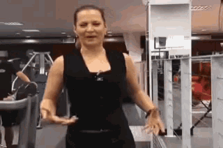 a woman in a black tank top is standing in a gym with her hands outstretched