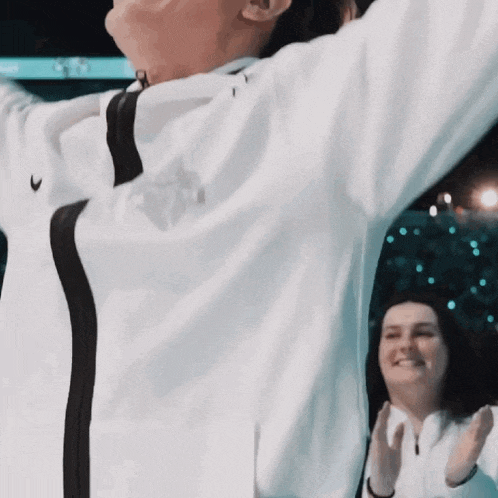 a man in a white nike jacket stands in front of a woman clapping