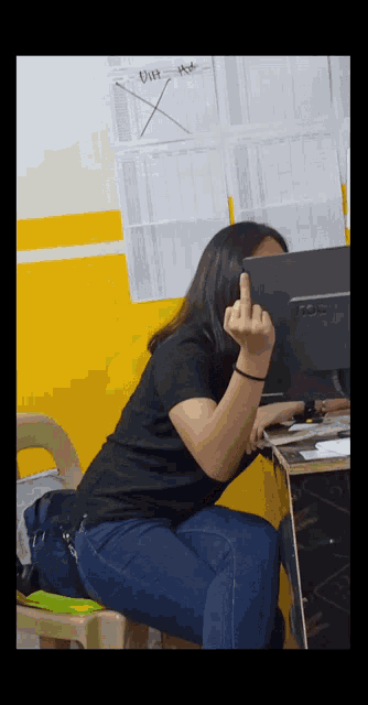 a woman sitting at a desk giving the middle finger in front of an aoc monitor