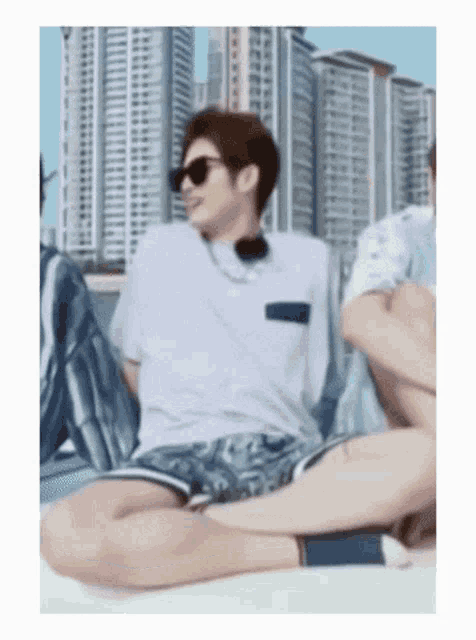 a man wearing sunglasses is sitting on the ground with his legs crossed in front of a city skyline .