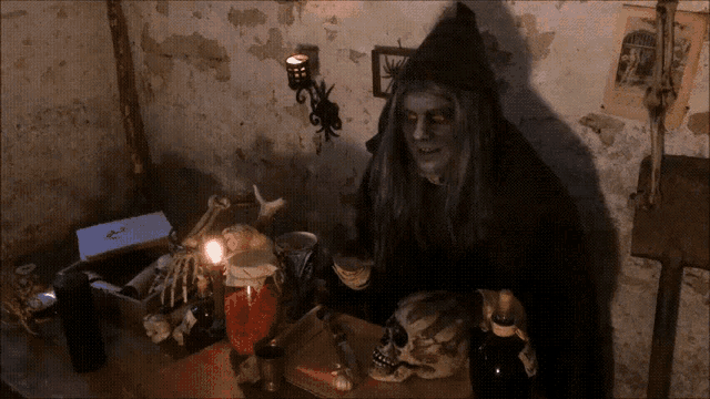 a man in a hooded cape stands in front of a table with a skull and bottles