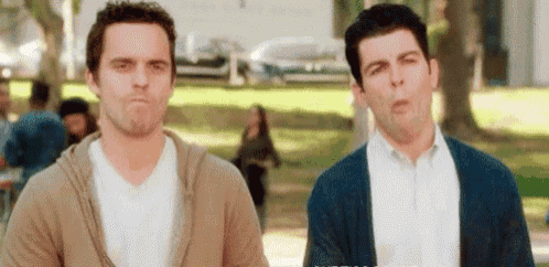 two men are standing next to each other in a park and making faces .
