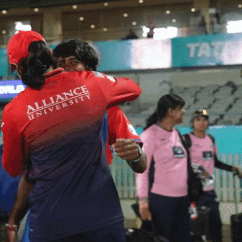 a woman wearing a red alliance university shirt is hugging a man