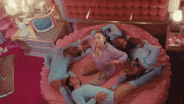 a group of women are laying on a bed in a pink room