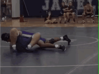 a referee is laying on the floor while two wrestlers are wrestling