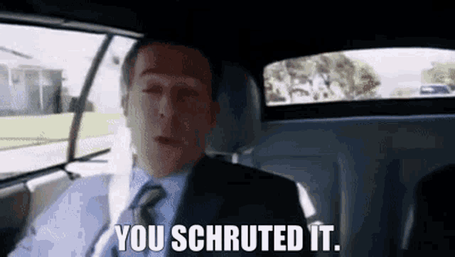 a man in a suit and tie is sitting in the back seat of a car and says you shruted it .