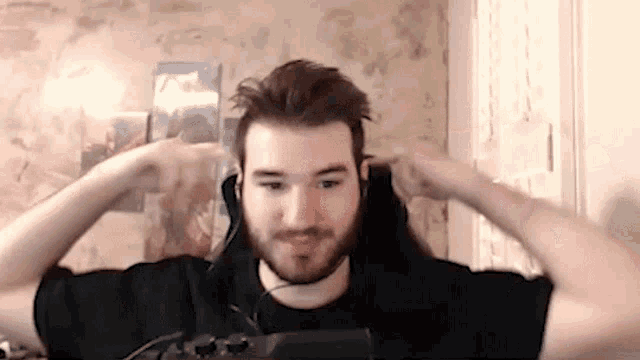 a man with a beard is wearing headphones and a headset while sitting in front of a computer .