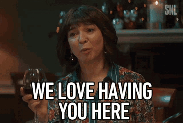 a woman is holding a glass of wine and saying we love having you here