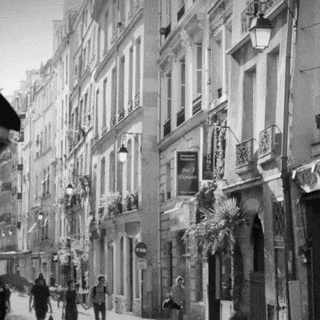 a black and white photo of people walking down a narrow street with a sign that says hotel voyageur on it