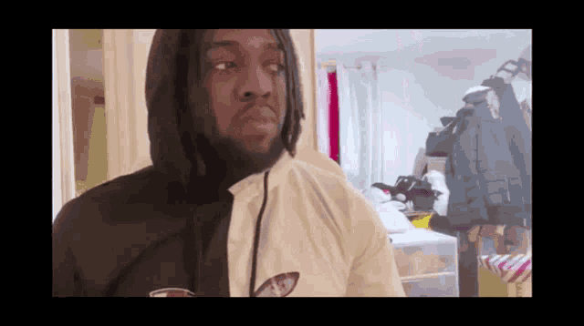 a man wearing a hoodie and a white shirt is standing in a messy room .