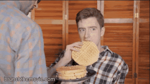 a man is eating a waffle while another man holds a stack of pancakes .