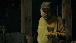 a man in a yellow shirt and hat is standing in a dark room holding a lighter .