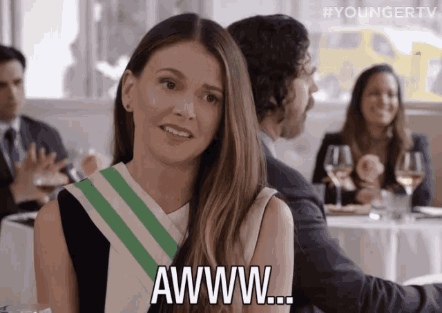a woman sitting at a table with a man behind her says awww