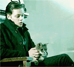 a man is sitting in a chair holding a small cat in his lap .