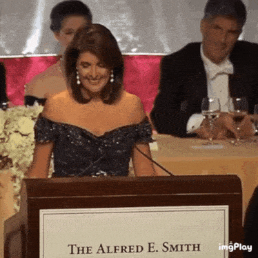 a woman is sitting at a podium with the name alfred e. smith on it