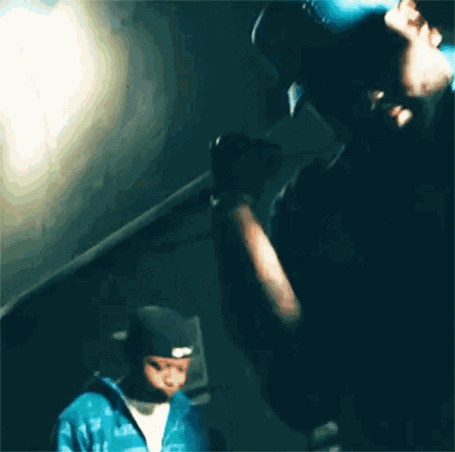 a man in a blue shirt is singing into a microphone while another man stands behind him