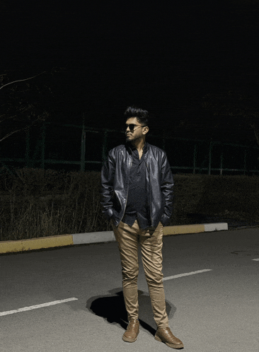 a man wearing sunglasses and a leather jacket stands on a street