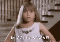 a little girl in a white dress is standing in front of a staircase and saying `` im gonna starve '' .