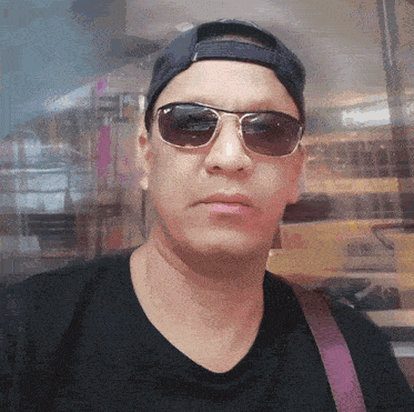 a man wearing sunglasses and a baseball cap stands in front of a window