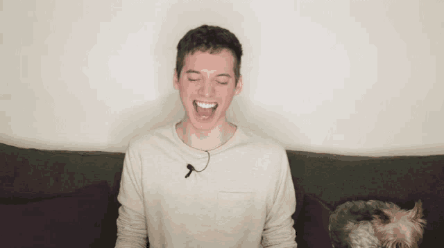 a young man is sitting on a couch with his mouth open and a dog laying next to him