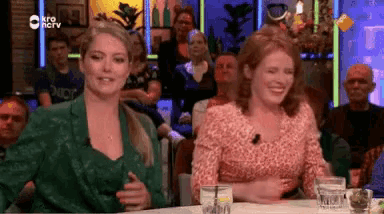 two women are sitting at a table in front of a crowd of people .