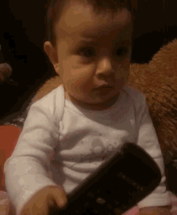 a baby in a white shirt is holding a black remote