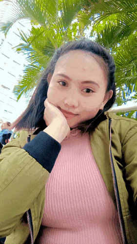 a woman wearing a pink sweater and a green jacket poses for a picture