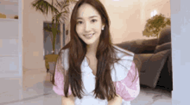 a young woman with long hair is standing in a living room and smiling .