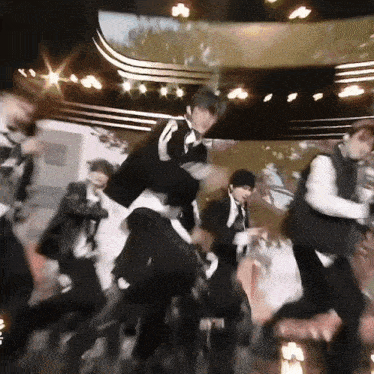 a group of men are dancing on a stage in front of a large screen .