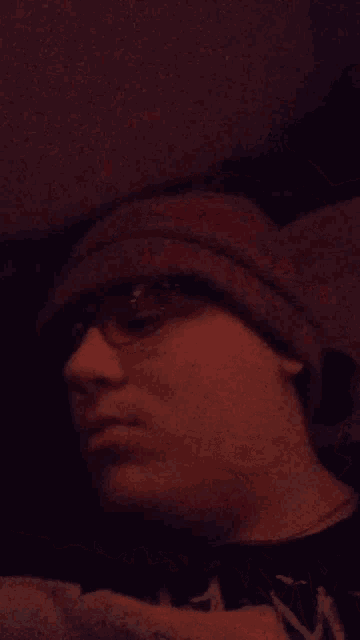 a man wearing glasses and a beanie looks at the camera with his eyes closed