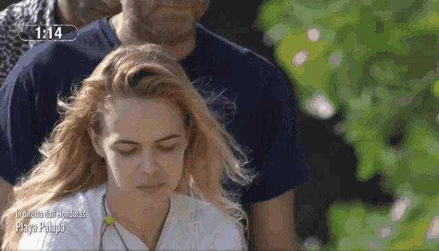 a woman in a white shirt stands in front of a screen that says 1:14