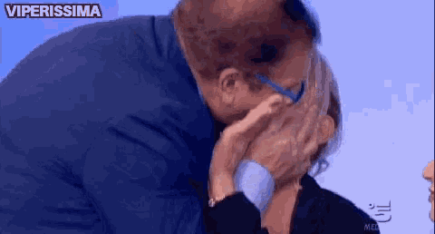 a man is kissing a woman on the cheek while wearing glasses and a blue shirt .